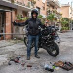 Motociclista pronto a controllare la sagoma dell'action cam sulla moto prima di partire, con cartelli di carico sporgente